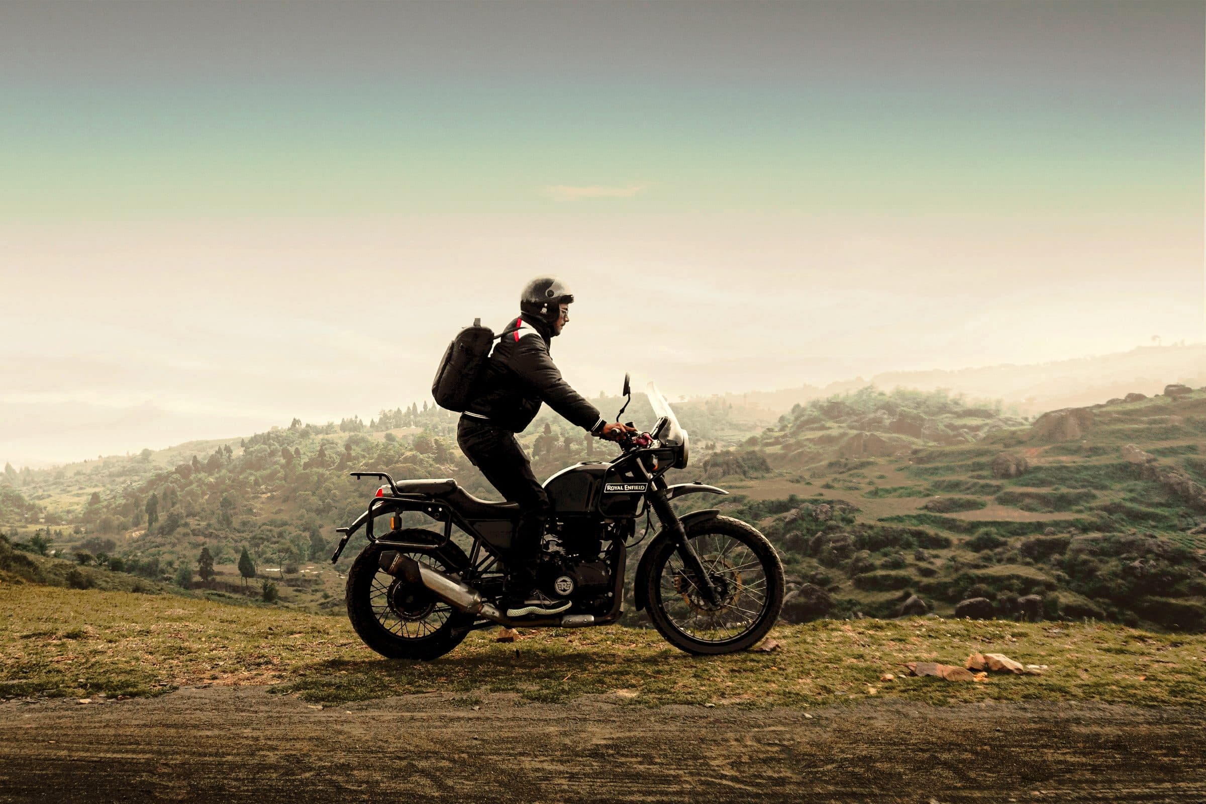 A rider on a Royal Enfield pausing on an open road above the hills